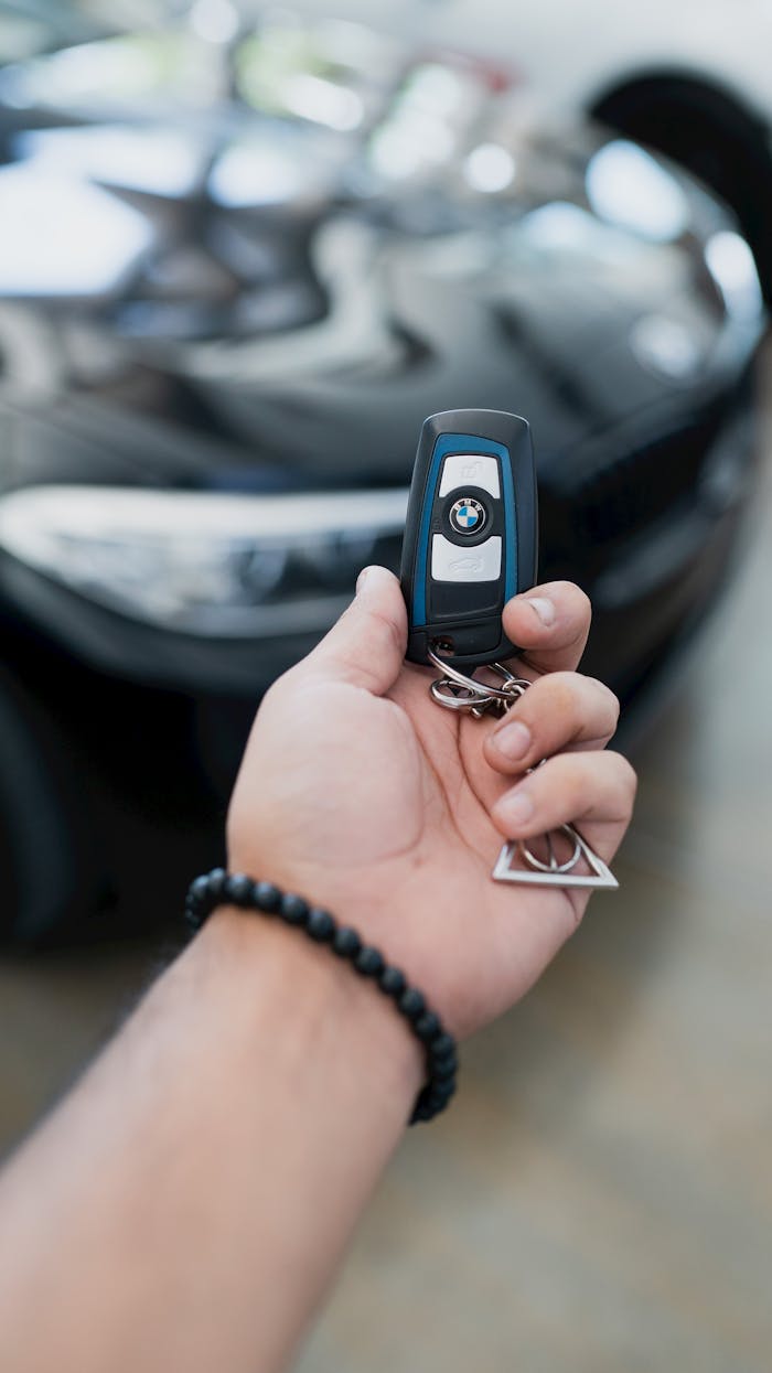 Close-up of a hand holding a luxury car key in focus, with the vehicle blurred in the background.